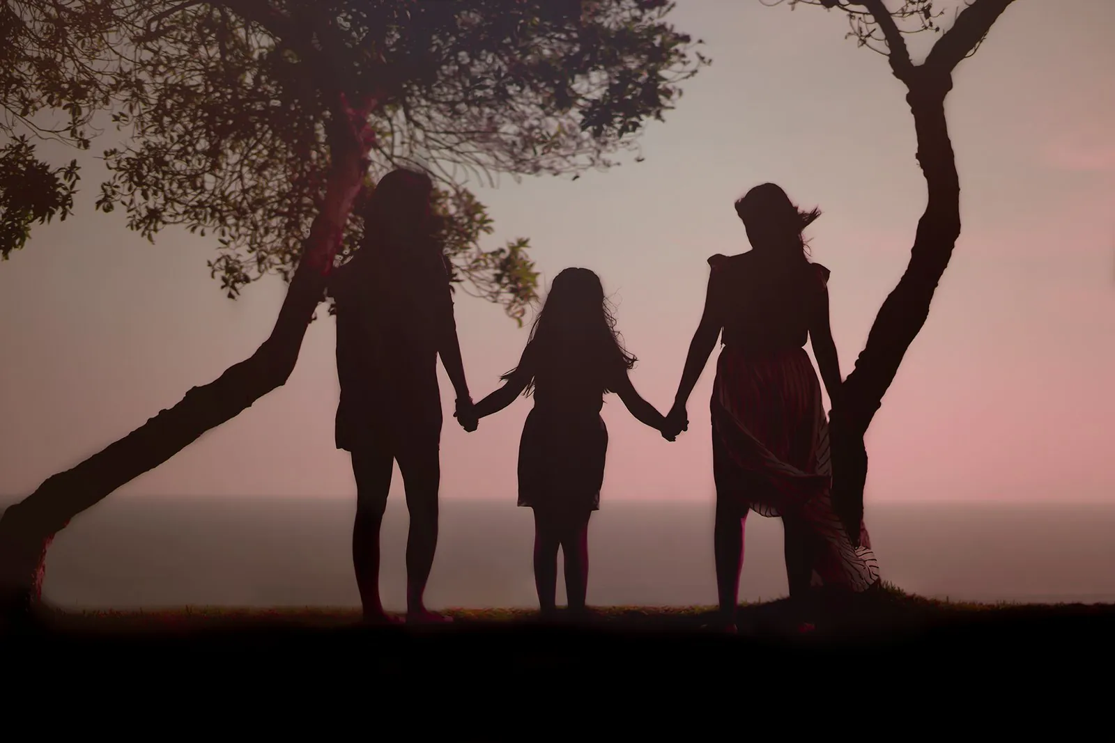 Tres personas tomadas de la mano frente al mar al atardecer